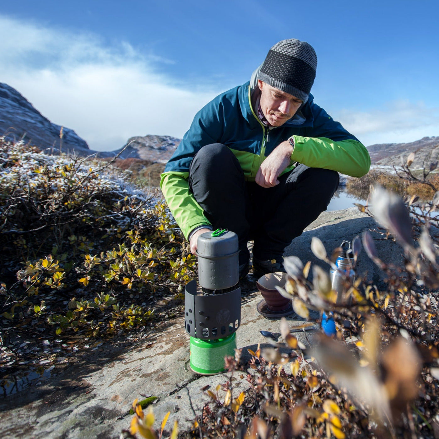 Zur Kategorie Campingkochen / Kochplatten: Mann bedient einen tragbaren Gaskocher in der Natur.