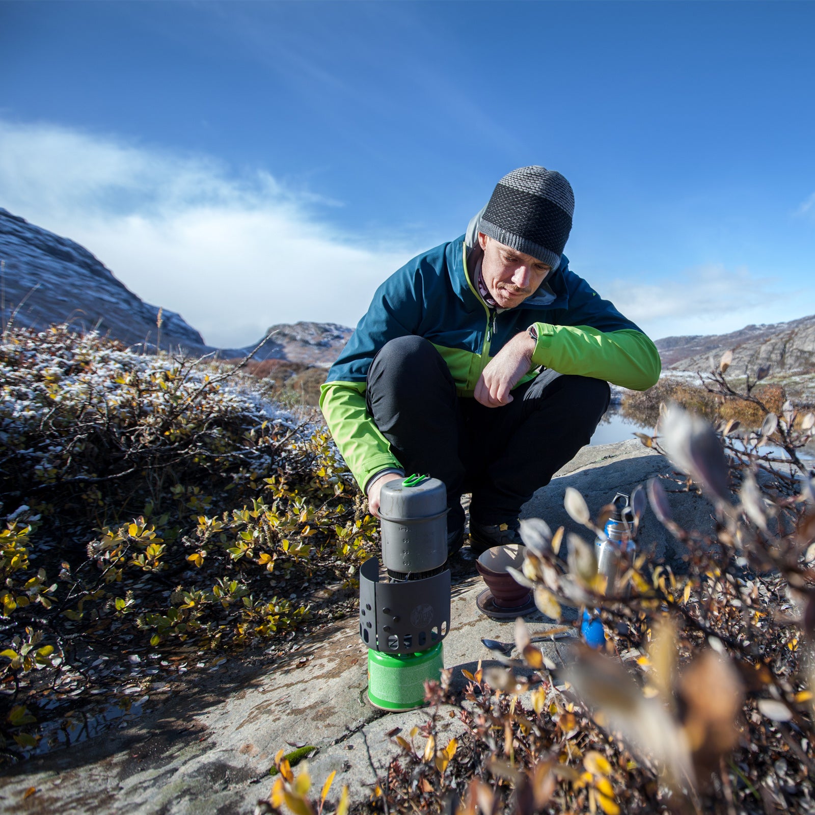 Zur Kategorie Campingkochen / Kochplatten: Mann bedient einen tragbaren Gaskocher in der Natur.