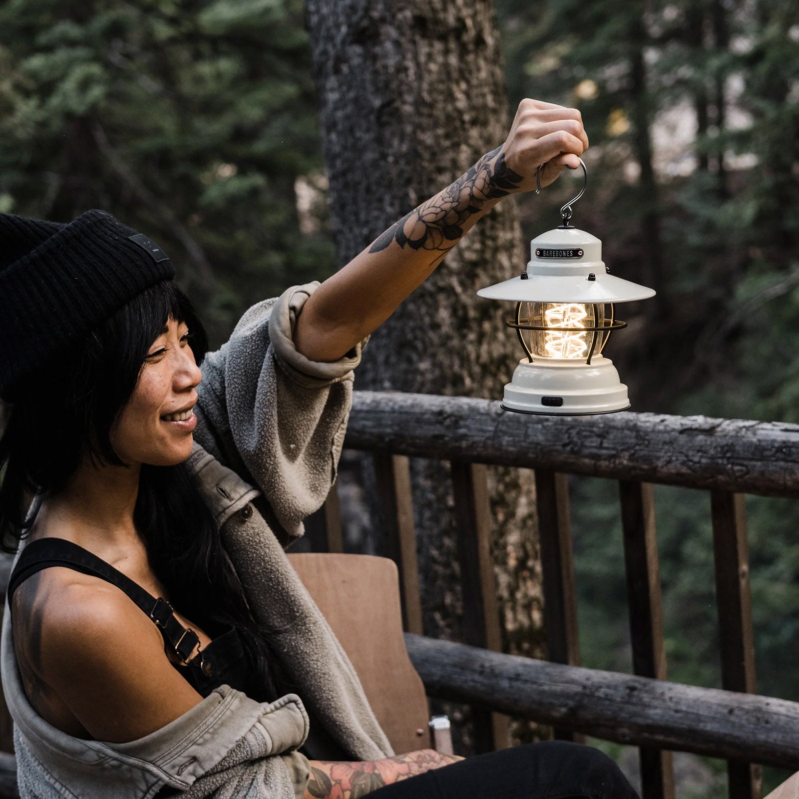 Zur Kategorie Beleuchtung: Weiße Barebones Campinglaterne steht auf Holztisch im Freien